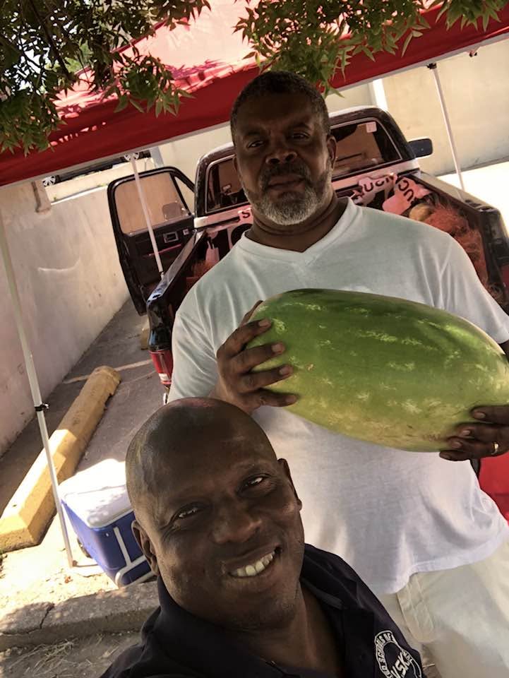 Longtime supporters under the tent holding a fresh watermelon