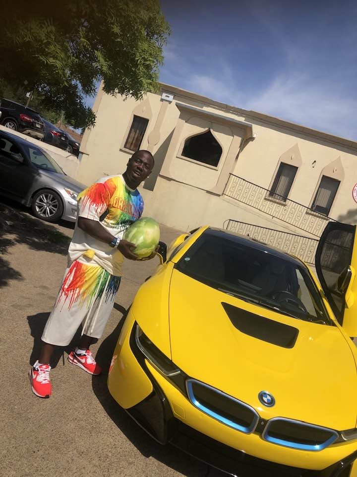 Supporter holding a fresh watermelon beside a yellow sports car